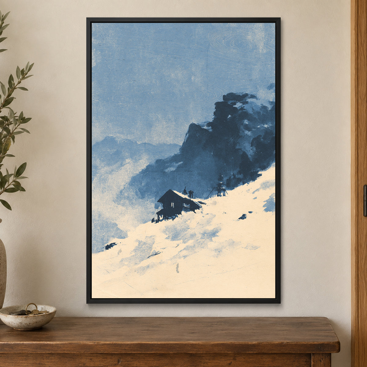 Lone Cabin Snow Slope framed canvas in a black floating frame on a cream wall above a wooden sideboard beside a door frame