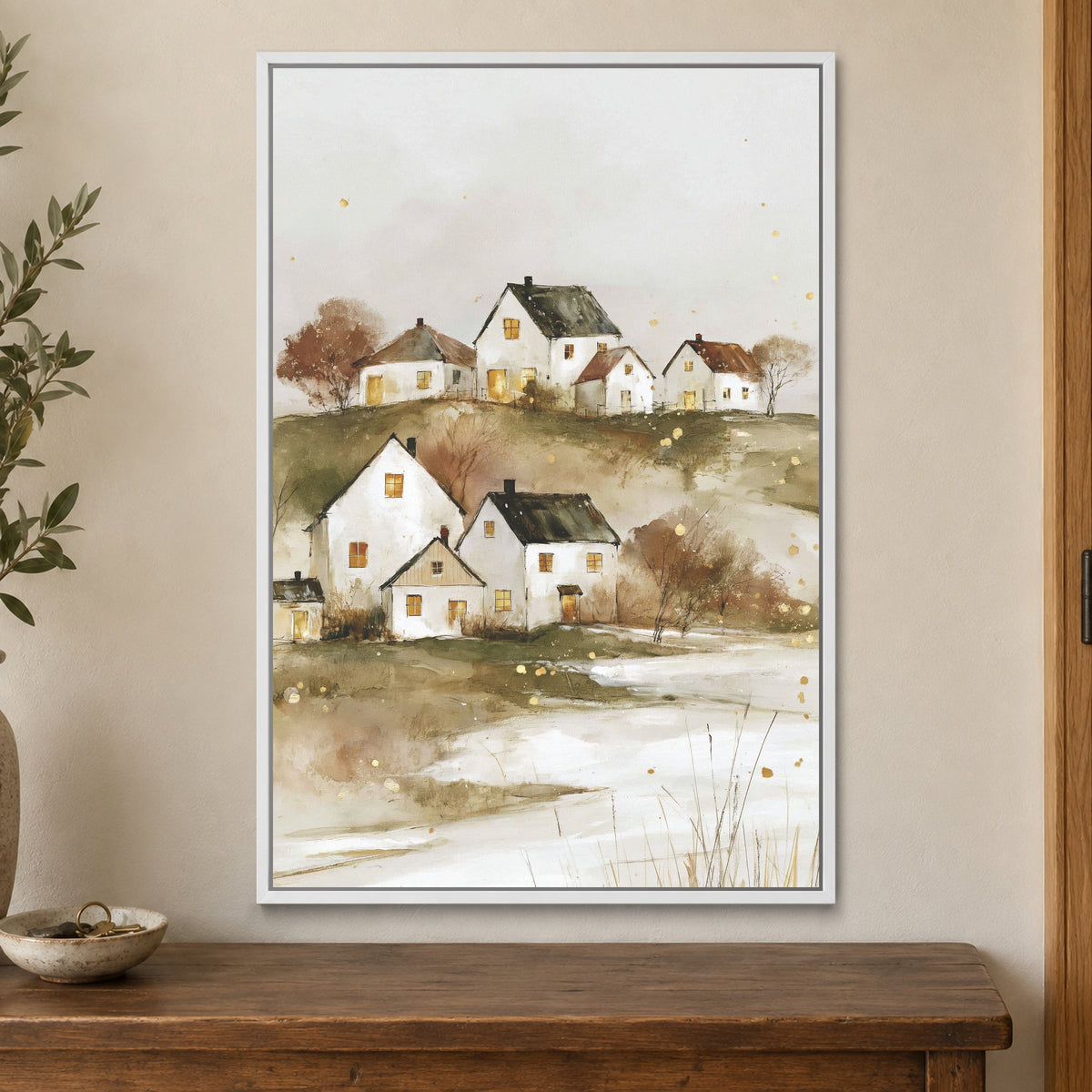 Canadian Prairie Farmhouses Winter framed canvas in a white floating frame on a cream wall above a wooden sideboard beside a door frame
