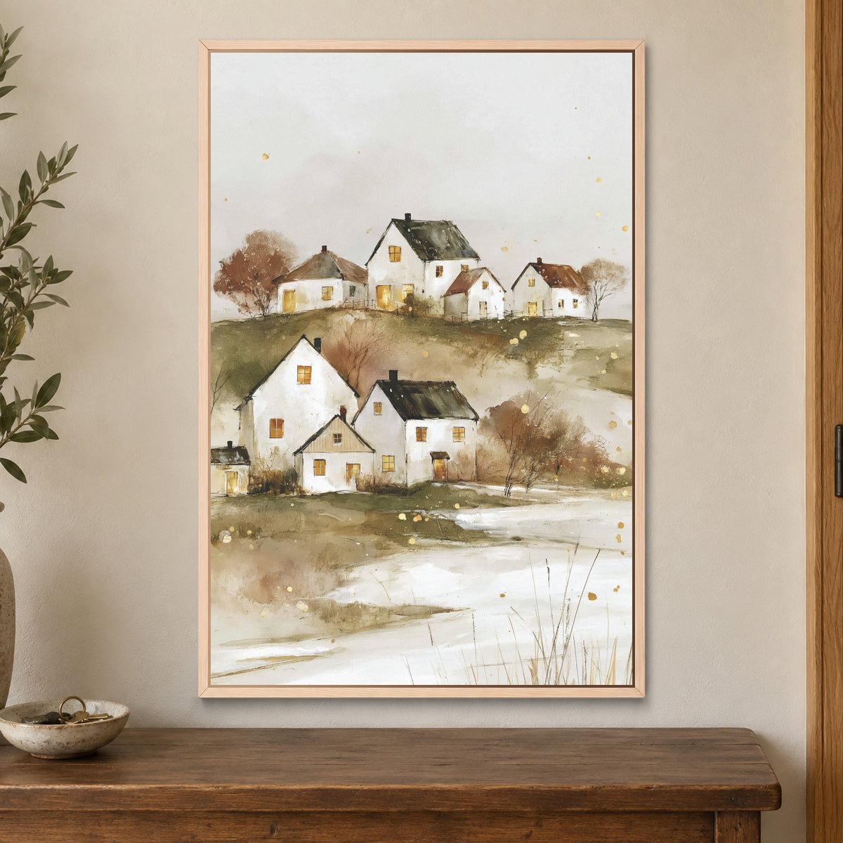 Canadian Prairie Farmhouses Winter framed canvas in a natural wood floating frame on a cream wall above a wooden sideboard beside a door frame