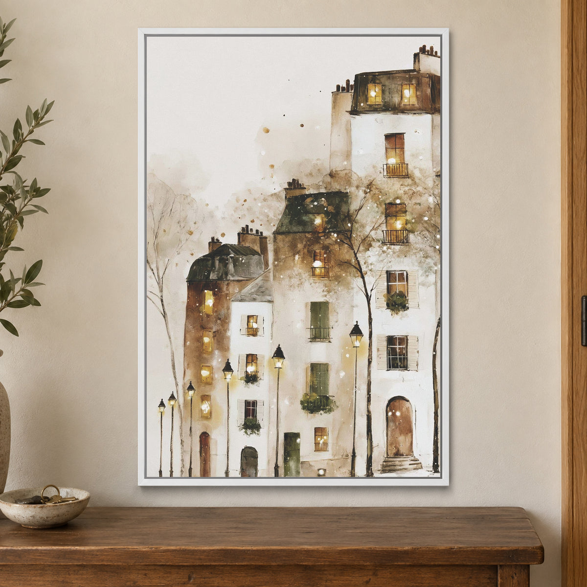 Paris Rooftops in the Snow framed canvas in a white floating frame on a cream wall above a wooden sideboard beside a door frame