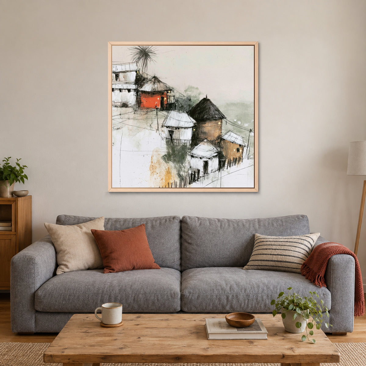 One Red Hut on the Slope framed canvas in a natural wood floating frame above a grey sofa with rust and striped cushions