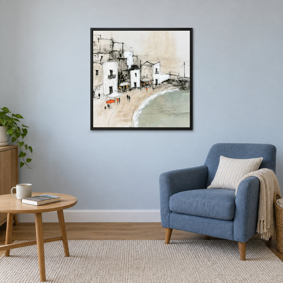 Whitewashed Seaside Village framed canvas in a black floating frame above a blue armchair and round wooden side table