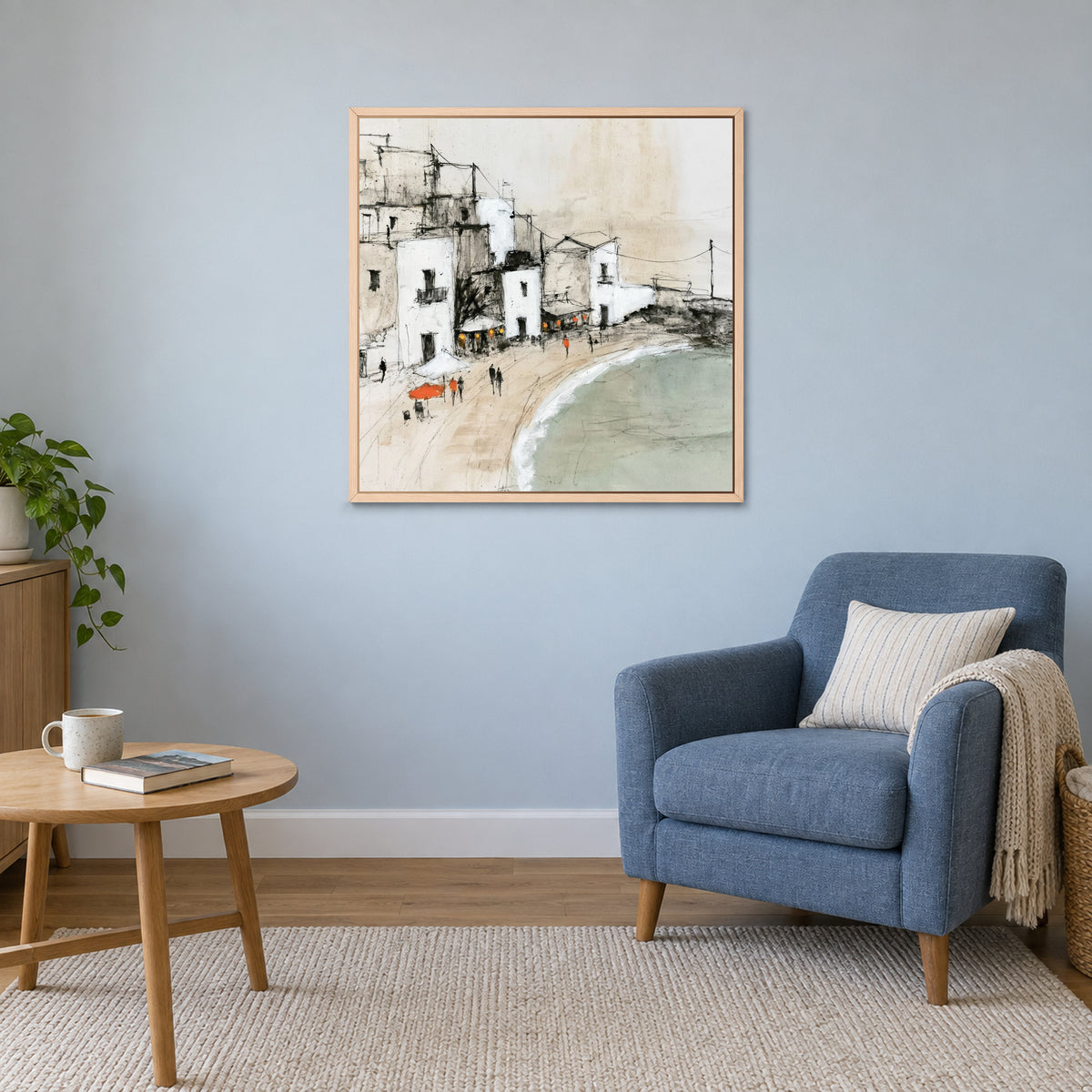 Whitewashed Seaside Village framed canvas in a natural wood floating frame above a blue armchair and round wooden side table