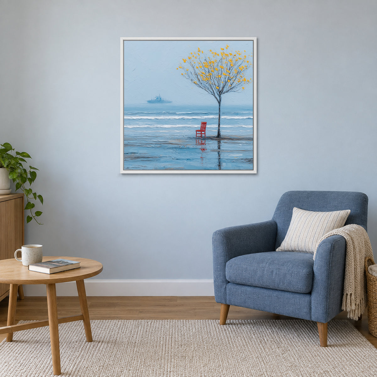A Red Chair by the Sea framed canvas in a white floating frame above a blue armchair and round wooden side table
